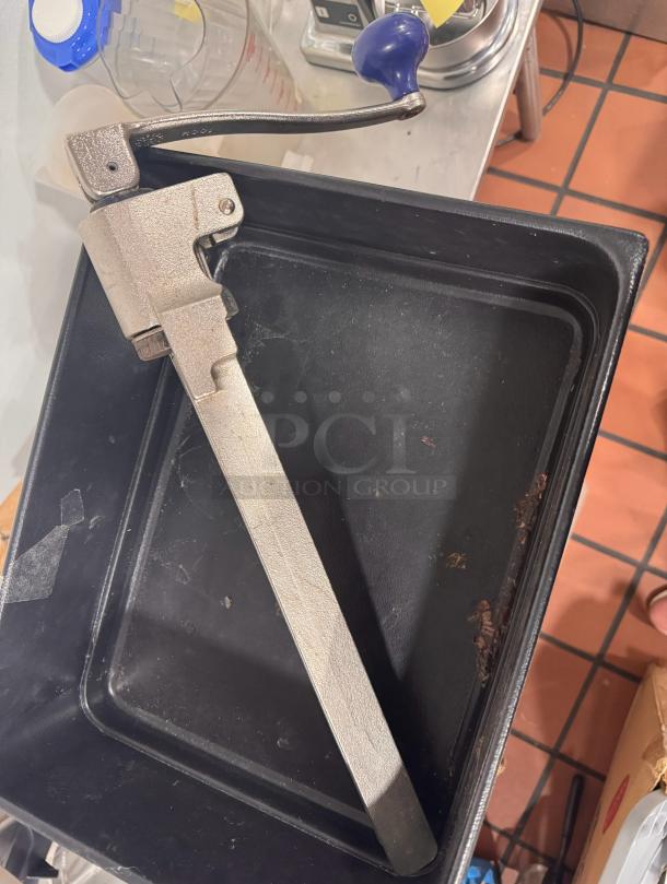 Heavy-duty metal can opener with a blue handle. Appears used, in good working condition. Suitable for commercial use.