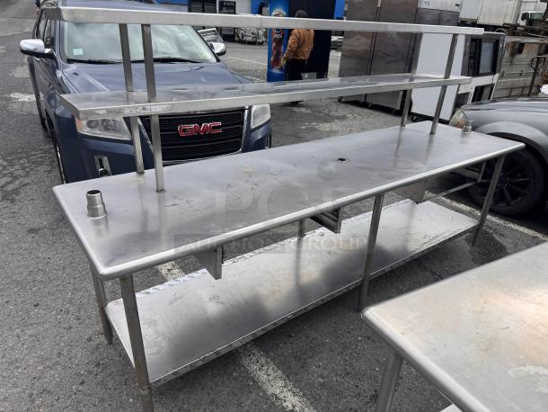 8ft stainless steel work table with overhead shelf, sturdy construction, visible wear, two exhaust ports, and under-shelf storage.