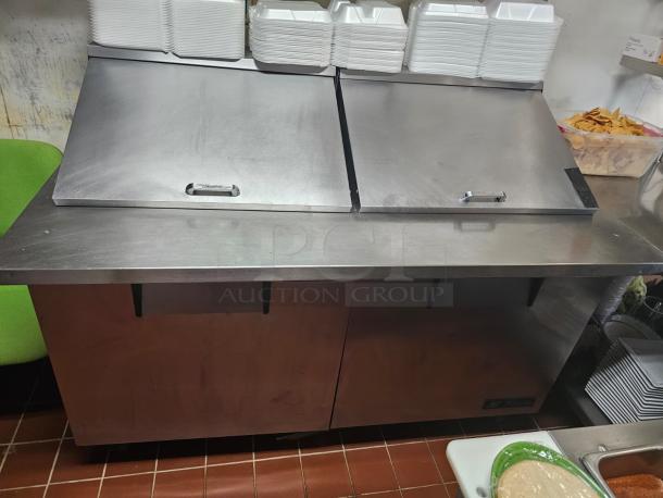 TRUE 60" prep table in stainless steel, tested and working. Features two flip-top lids and storage area. Good condition.