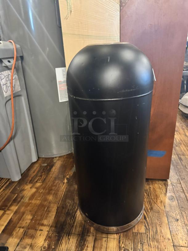 Black cylindrical trash can in used condition with a dome lid. Scuff marks visible on the surface.