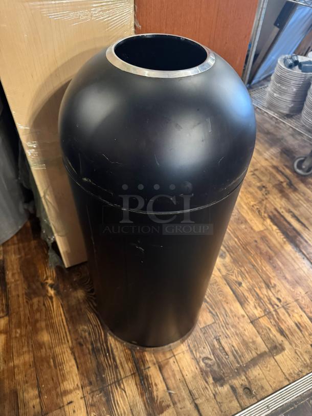 Black cylindrical trash can with a domed lid and stainless steel rim. Used condition, minor surface scratches visible.