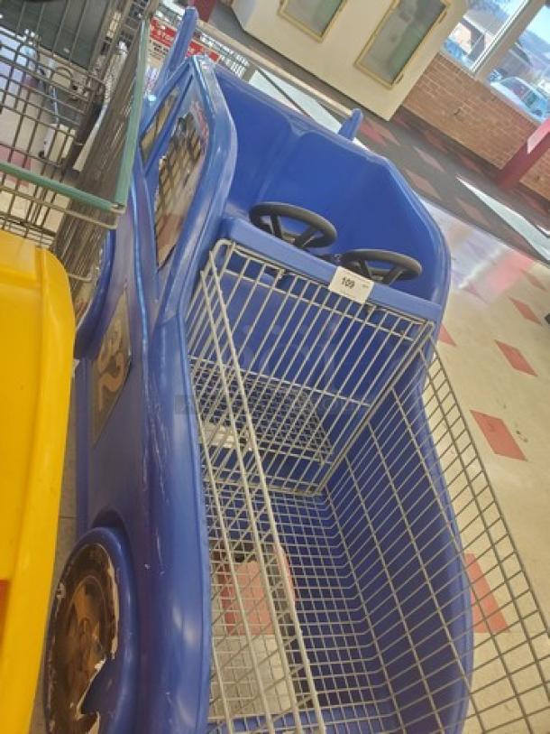 Blue race car-themed shopping cart with dual steering wheels, metal basket, and child seating area, labeled as item 189.