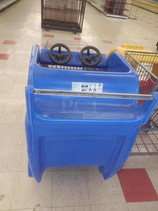 Blue race car shopping cart with dual steering wheels. Shows light wear. Safety label with usage instructions visible on front panel.