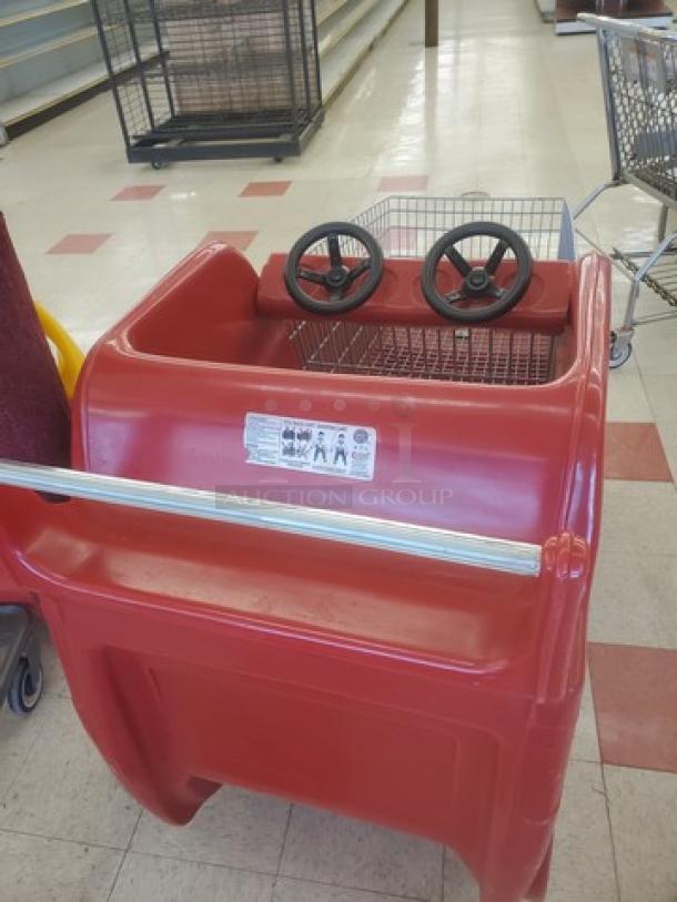 Red race car shopping cart with dual steering wheels, mesh basket, and visible safety label. Used condition.