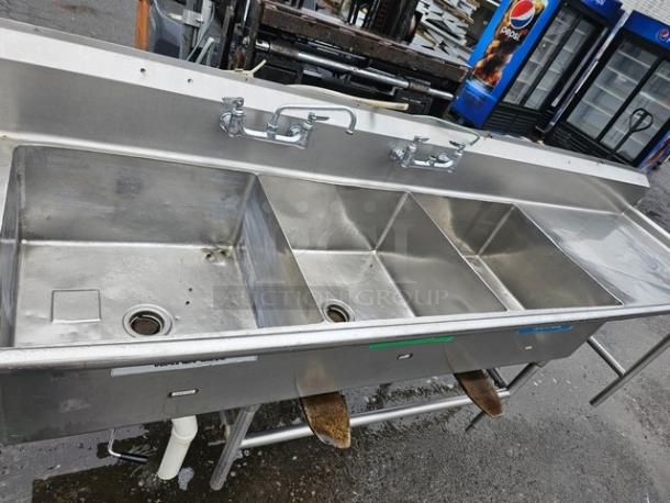 140" stainless steel three-compartment sink with dual drainboards, featuring dual faucets, in used condition.