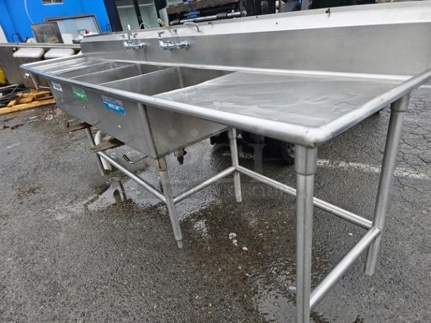 140" stainless steel three-compartment sink with dual drainboards, commercial-grade, pre-owned, visible tap fixtures.