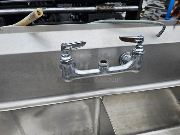140" stainless steel three-compartment sink with dual faucets, integrated drainboards, in used condition.