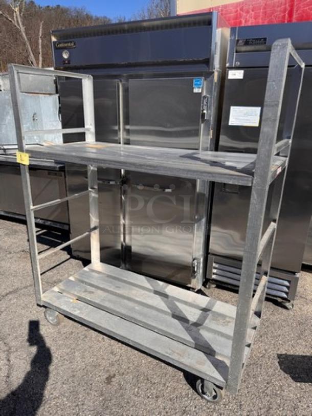 Heavy-duty aluminum shelving unit with two shelves, industrial casters, showing slight wear, suitable for storage or transport.