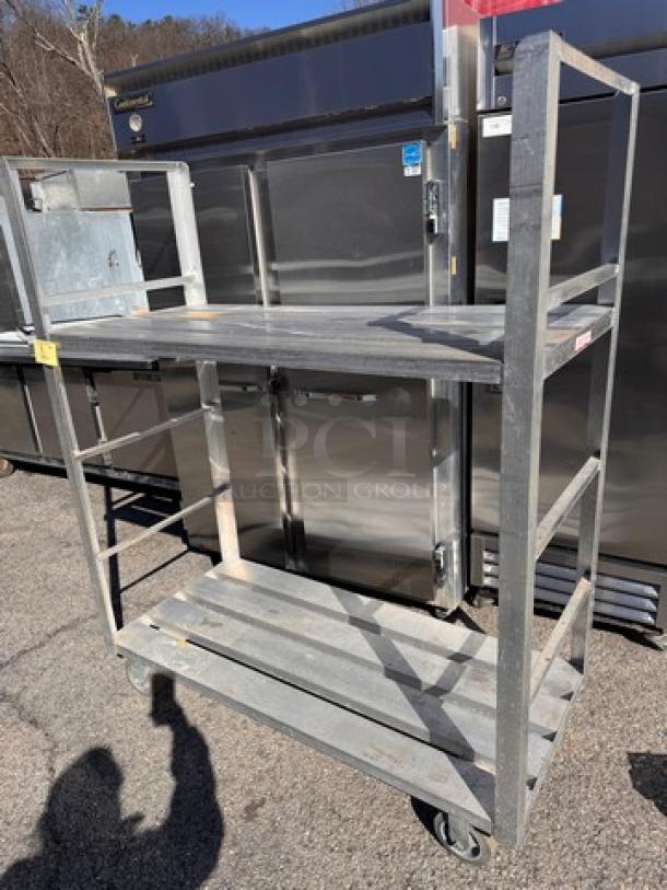 Heavy-duty aluminum shelving unit with three tiers, sturdy construction, casters for mobility, in good condition.