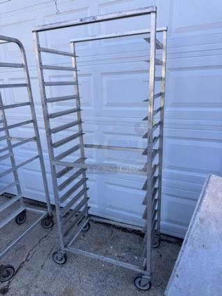 Aluminum pan rack with multiple slots, mounted on wheels, used condition. Suitable for commercial kitchens, sturdy frame.