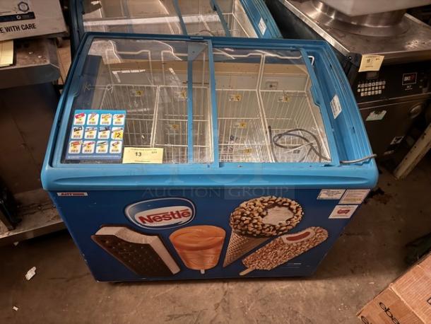 AHT RIO S 100 ice cream freezer with sliding glass top, blue exterior, Nestlé branding, multiple compartments. Minor wear visible.