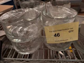 Lot of 9 clear glass bowls wrapped in plastic, good condition, on a metal shelf. Auction tag reads "46 QTY."