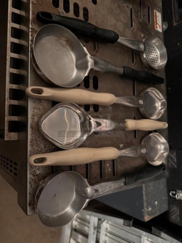Set of six food portion/serving spoons with metal heads and varied handle designs, showing signs of use.