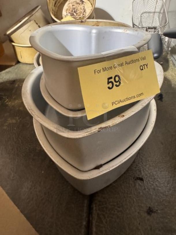 Stack of four metal baking pans, varying sizes, slightly used. Yellow auction tag numbered 59 from PCI Auctions visible.