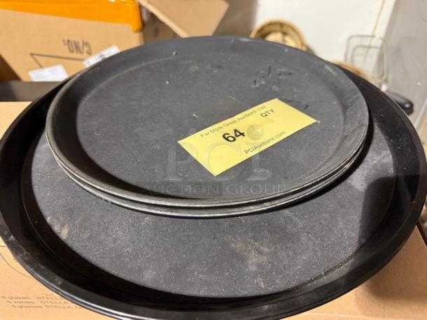 Stacks of round black trays with visible wear and tear. A yellow label marked "64 QTY" is placed on top.