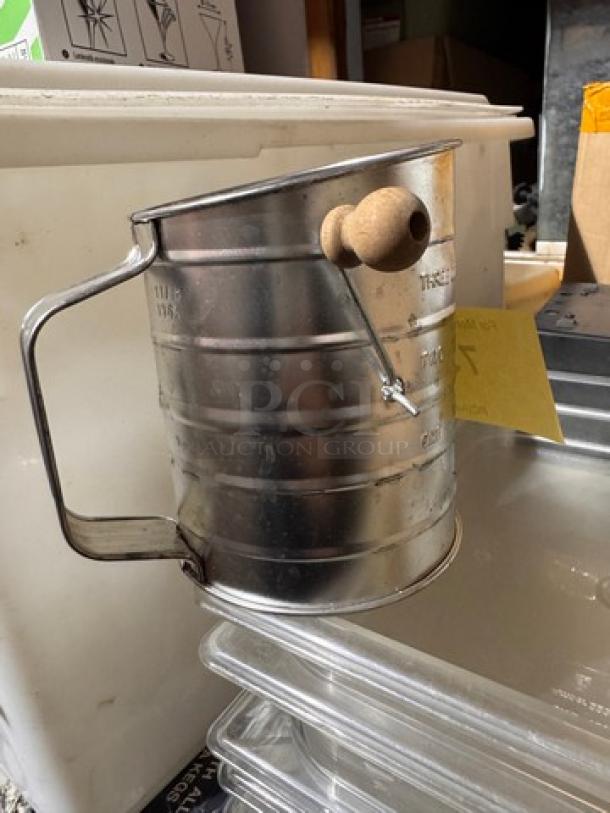 Stainless steel flour/sugar sifter with a wooden handle, manual crank. Used condition, no visible brand markings.