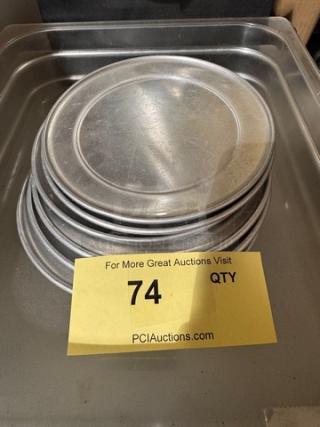 Small stack of round aluminum pizza pans, gently used, with a yellow tag displaying item number 74 and auction site details.