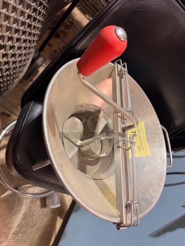 Stainless steel food mill with red handle, used condition, mesh strainer, rotating blade; includes attached yellow tag.