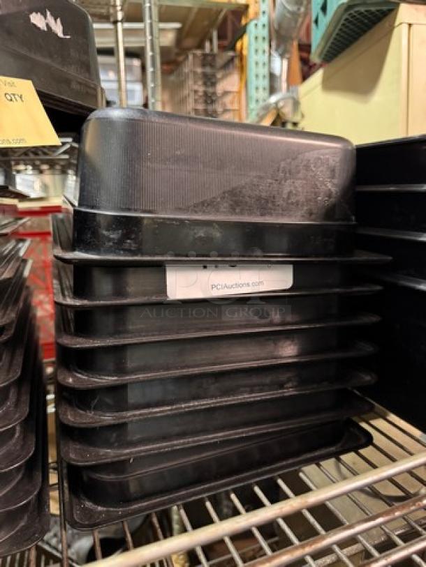 Stack of black 1/2x4IN food pans with visible label "PCIAuctions.com," in used condition on metal rack.