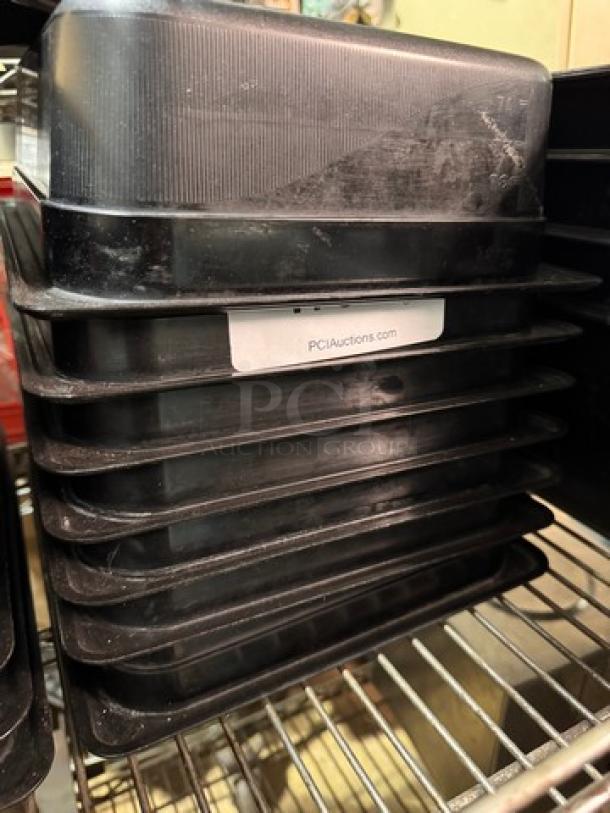 Stack of black 1/2x4IN food pans, model BIDX7, in good condition, with PCI Auctions label visible.