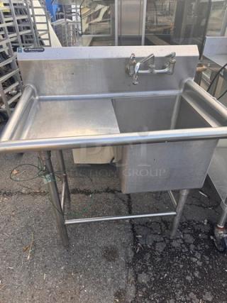 Stainless steel sink, commercial grade, with high backsplash and attached faucet. Freestanding on sturdy legs. Used condition.