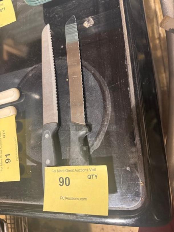Lot of 2 serrated knives with black handles, signs of use, auction tag reads "90 QTY", sold as one item.