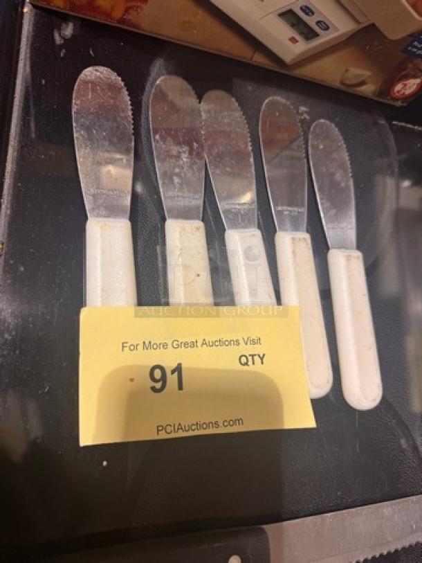 Lot of 5 metal spreader knives with white handles. Used condition. Auction tag labeled "91."