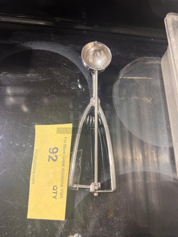 Stainless steel squeeze disher, features ergonomic handle and spring mechanism, used condition. Auction tag number 92 visible.