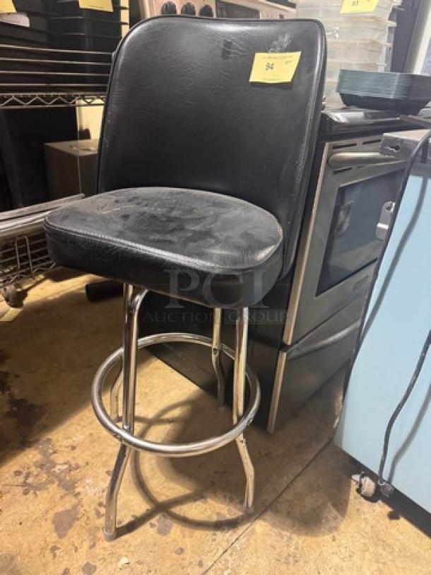 Black leather stool BIDX2 with chrome legs and footrest, showing signs of wear, tag indicating item number 94.