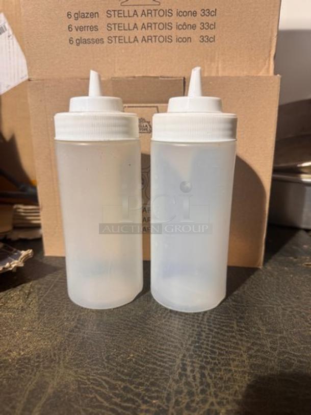 Two translucent squeeze bottles, model BIDX2, with white caps, in good condition; background shows Stella Artois box.