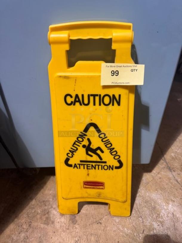 Yellow folding CAUTION sign with multilingual warning text and slip hazard icon. Brand mark at bottom. Good condition.