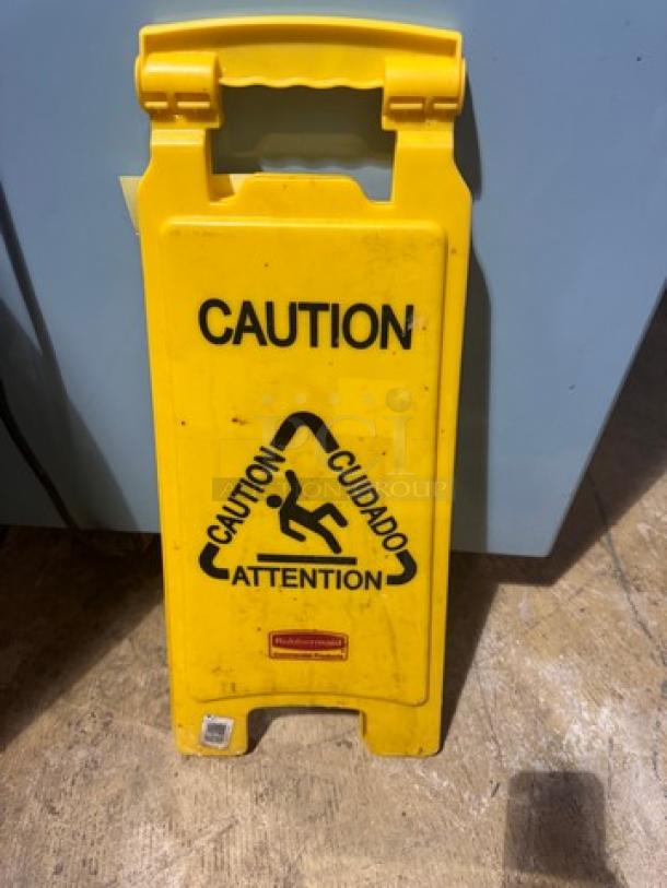 Yellow folding "CAUTION" sign with bilingual warning text and slip hazard symbol, in used condition.