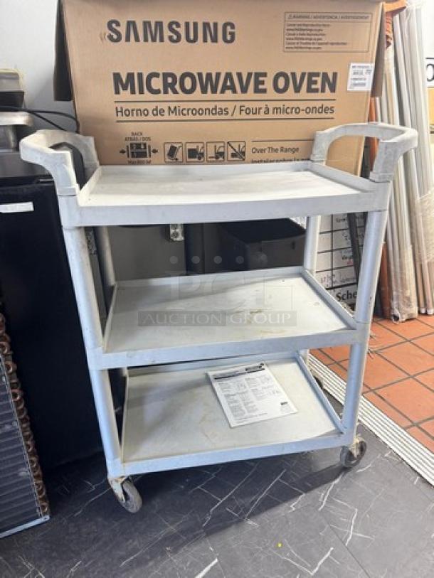 Gray utility cart with three shelves, used condition, caster wheels for easy mobility. Samsung microwave box in background.