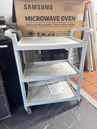 Gray utility cart with three shelves, used condition, caster wheels for easy mobility. Samsung microwave box in background.