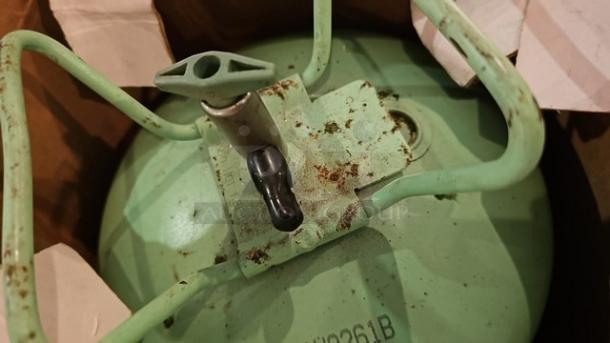 Green refrigerant R22 cylinder with visible valve and surface rust, partially in a cardboard box. Model #2261B.