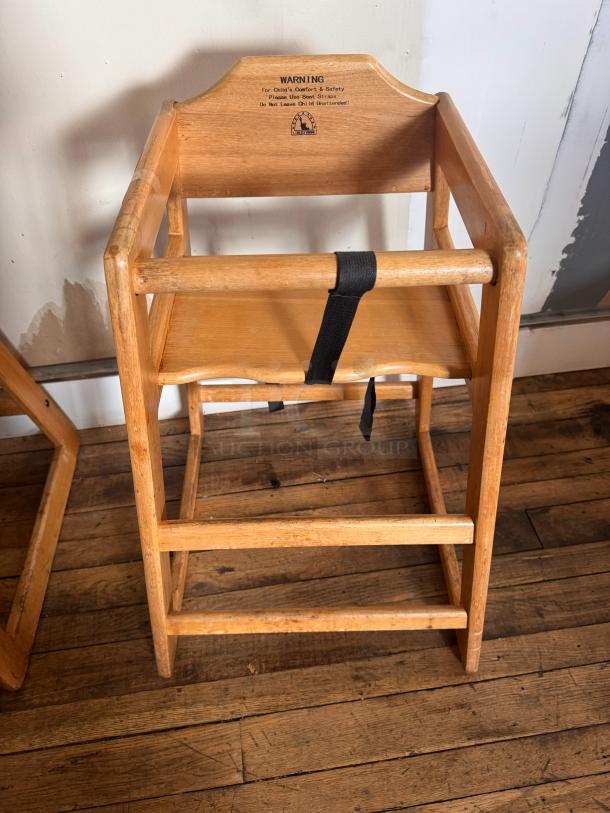 Wooden high chair with safety strap, visible wear. Label warning for child's comfort and safety.