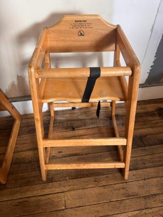 Wooden high chair with safety strap, visible wear. Label warning for child's comfort and safety.