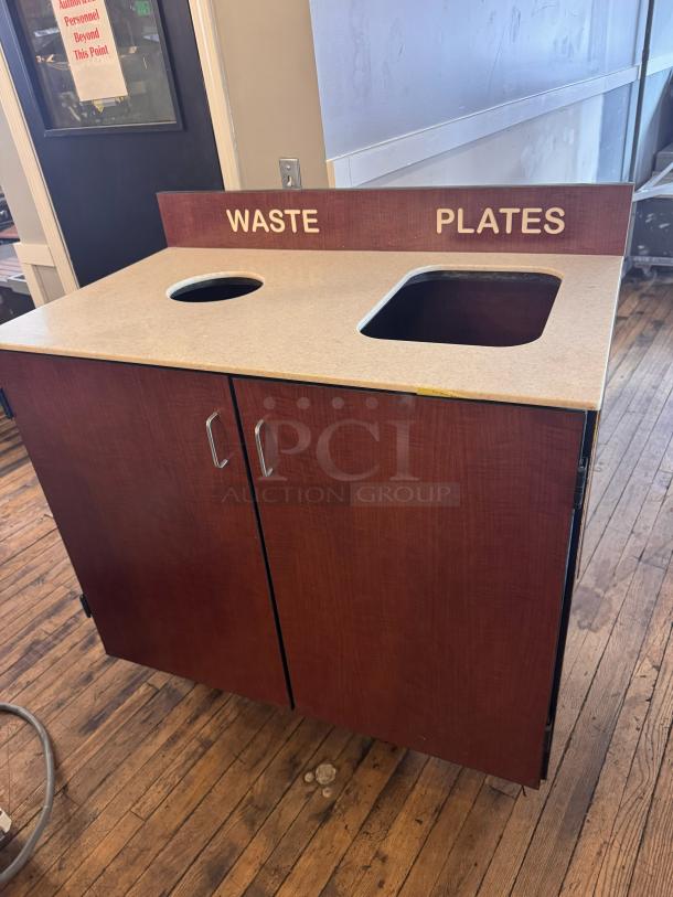 Wooden trash receptacle with designated waste and plates slots, laminate top, dual doors; good condition.