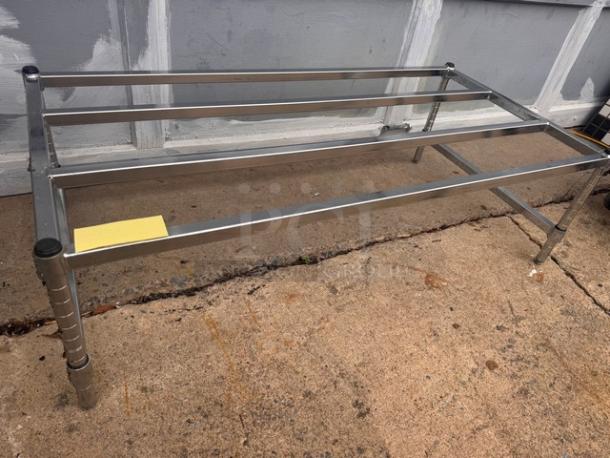 Stainless steel dunnage rack, four-bar design, sturdy construction, outdoor setting, minor wear visible, ideal for storage.