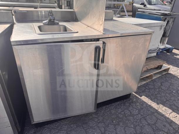Stainless steel stand with small sink, featuring a single faucet and storage cabinet below. Good condition, durable design.