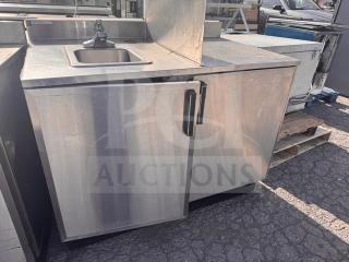 Stainless steel stand with small sink, featuring a single faucet and storage cabinet below. Good condition, durable design.