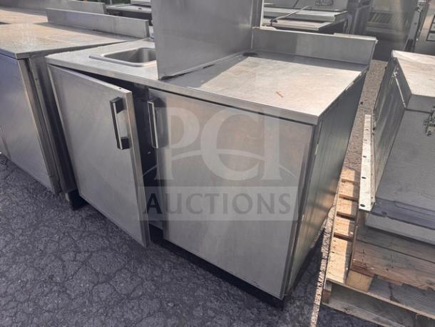 Stainless steel stand with small sink, double doors, and sturdy handles. Used condition, ideal for commercial kitchens.