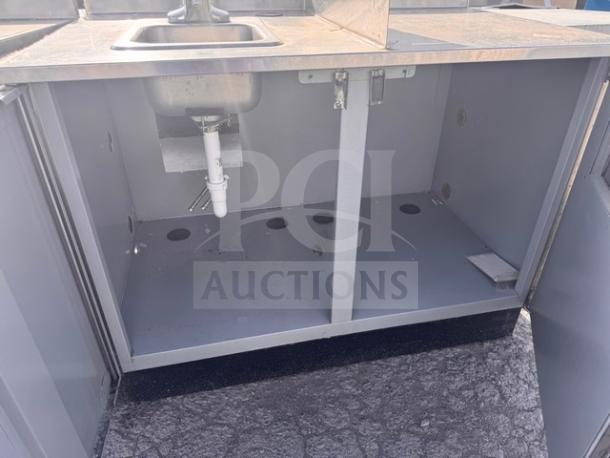 Stainless steel stand with small sink, open cabinet storage, clean condition, visible plumbing fixtures, grey finish.