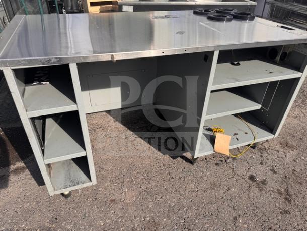 Stainless steel work stand with multiple shelves in used condition, featuring a flat top surface and open storage compartments.