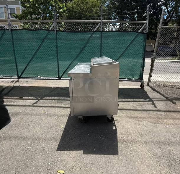 Delfield 18672PTLP 72" refrigerated pizza prep table, stainless steel, two doors, raised rail, on wheels, outdoor photo.