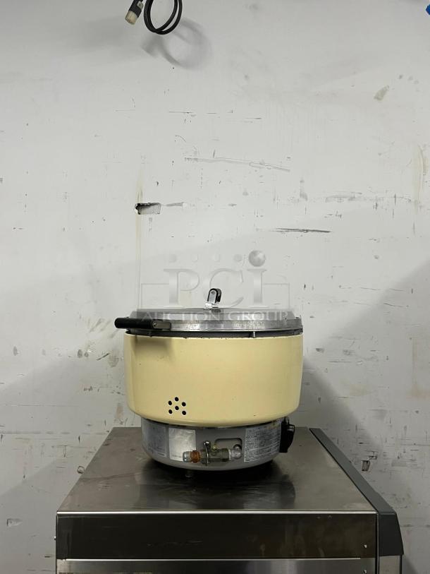 Rinnai RER55ASN 55-cup commercial natural gas rice cooker on metal surface, beige exterior, visible gas fittings.