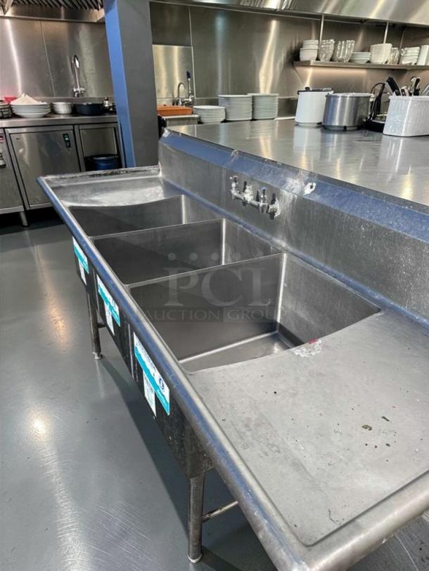 Commercial 3-compartment stainless steel sink with dual drainboards, NSF-certified, immaculate condition, ready for installation.