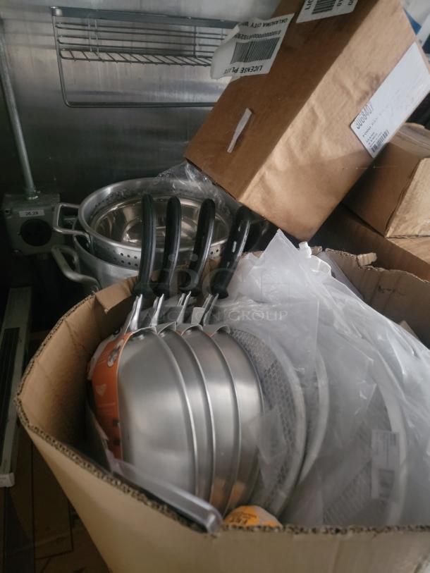 Boxed kitchenware, including stacked frying pans and a pot, inside a Rock Solid Cargo 24' mobile kitchen trailer.