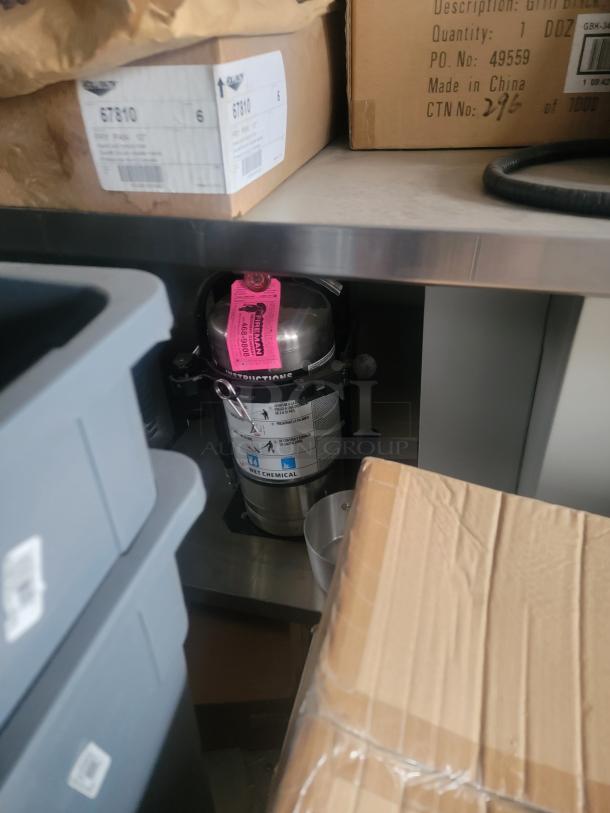A wet chemical fire extinguisher on a shelf, with cardboard boxes and plastic bins nearby.