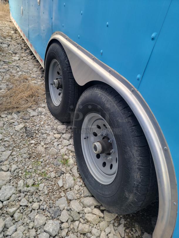 Blue Diamond Cargo mobile kitchen trailer, side view showing dual axles and tires on gravel.